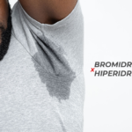 Homem negro com o braço levantado, vestindo uma camisa cinza que está manchada de suor.