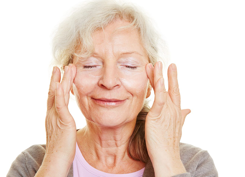 Imagem de uma mulher de idade fazendo massagem facial.