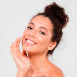 Imagem de uma mulher morena sorrindo e com uma mão no rosto.